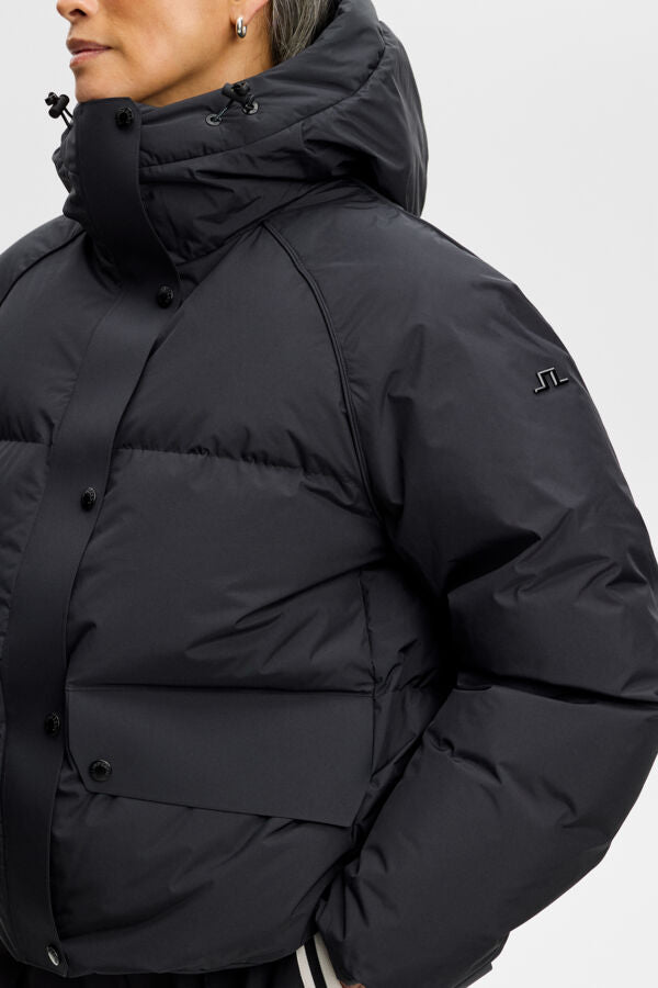 Lea Down Jacket in black, close-up view showing the hood, snap placket, and Bridge logo on the sleeve.