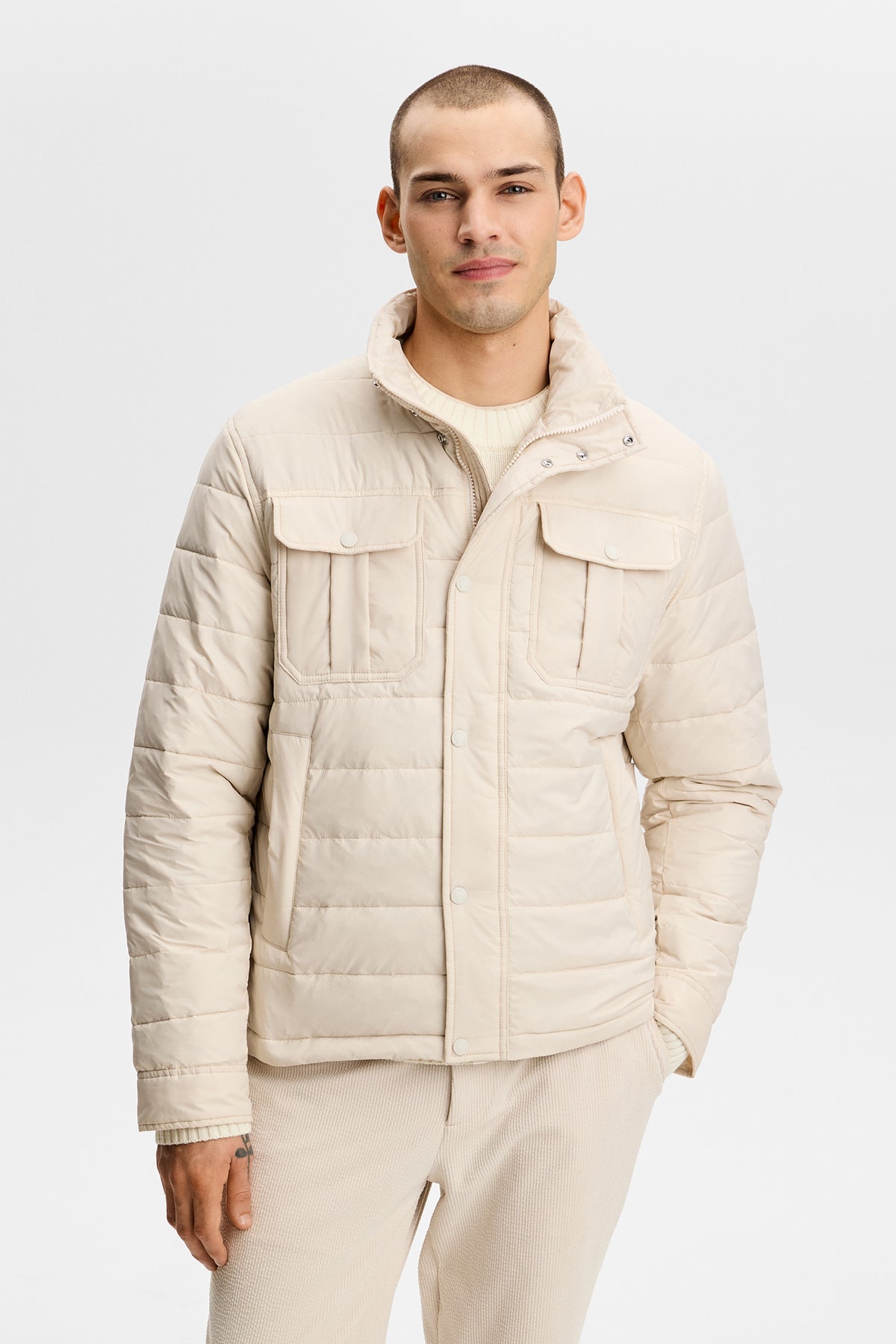Model wearing the Bailey Light Padded Jacket in Moonbeam with quilted channels and chest flap pockets.