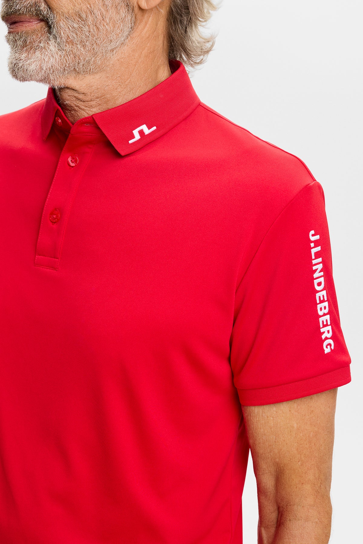Close-up: Red Tour Tech Polo with embroidered Bridge logo on the collar and J.LINDEBERG sleeve text.