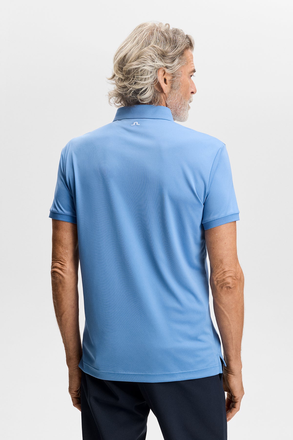 Tour Tech Polo in Riviera blue, back view showing the white embroidered Bridge logo below the collar.