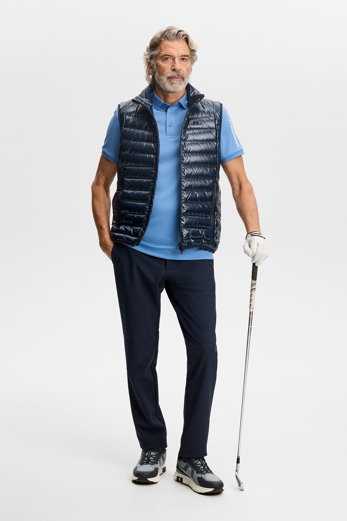 Model wearing the Tour Tech Polo in Riviera under a quilted vest in a studio setting.