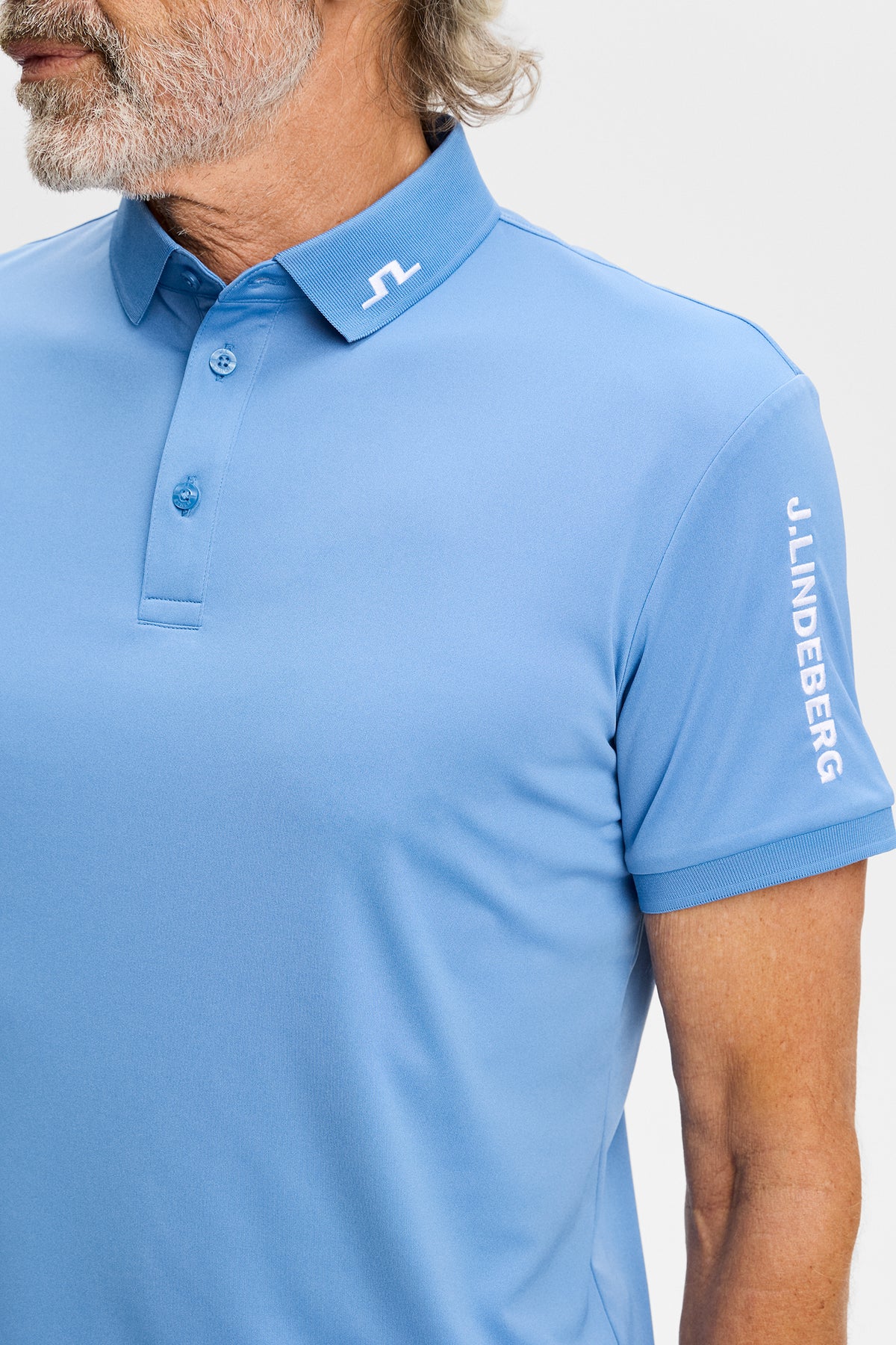 Close-up of the Tour Tech Polo in Riviera blue, showing the embroidered Bridge logo on the collar and sleeve.