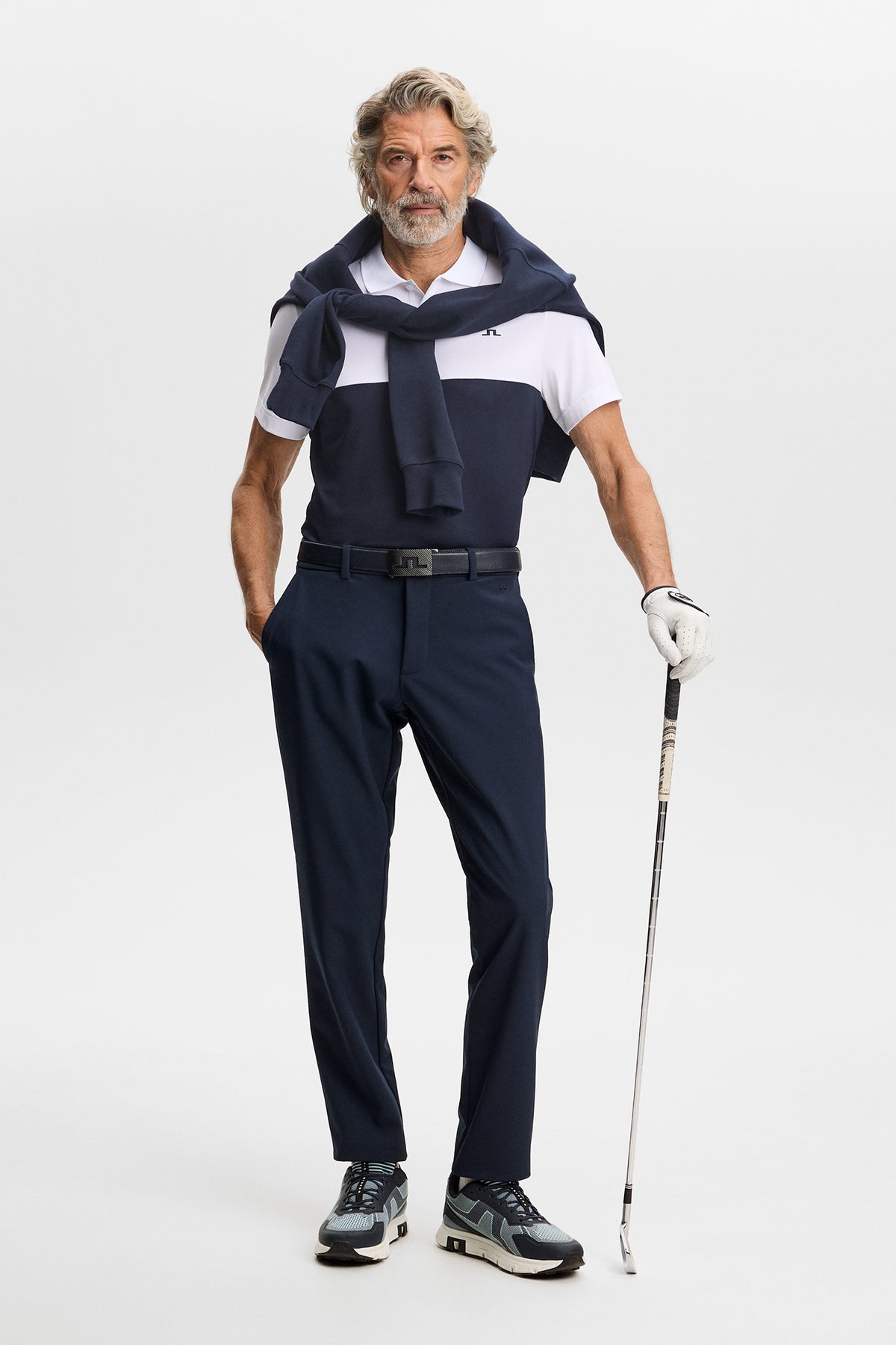 Model wearing the Mitch Bonded Players Pant in JL Navy with a polo and golf club in a studio setting.